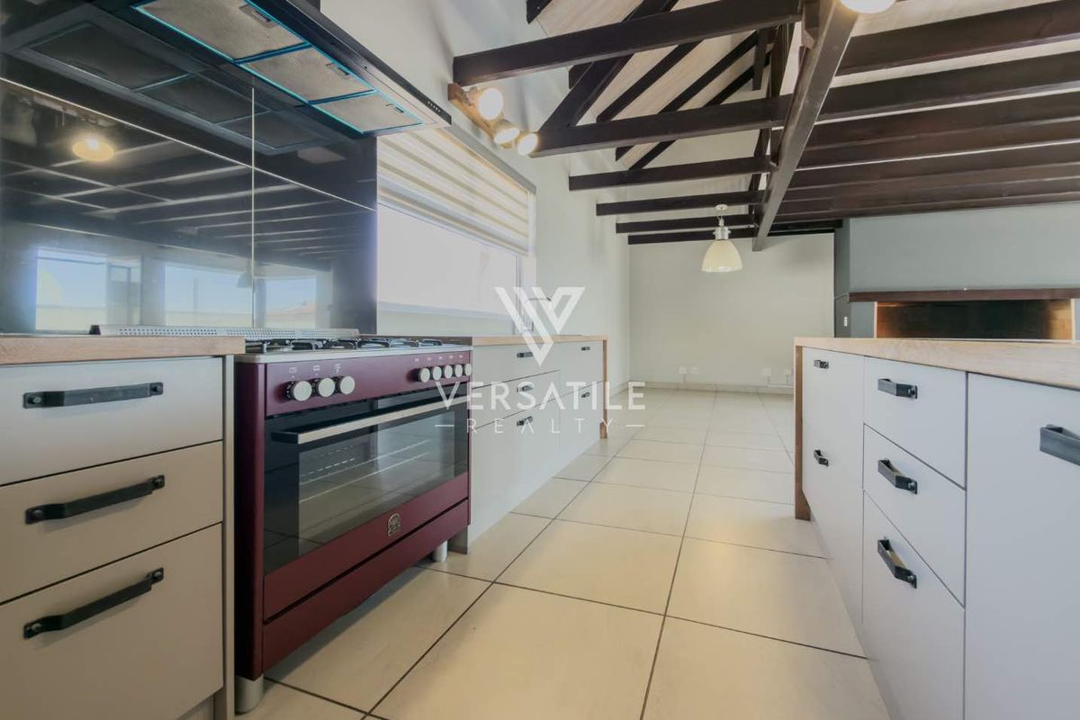 Modern kitchen featuring a gas stove, extractor fan, kitchen island, and exposed timber ceiling beams with neutral tiled flooring.