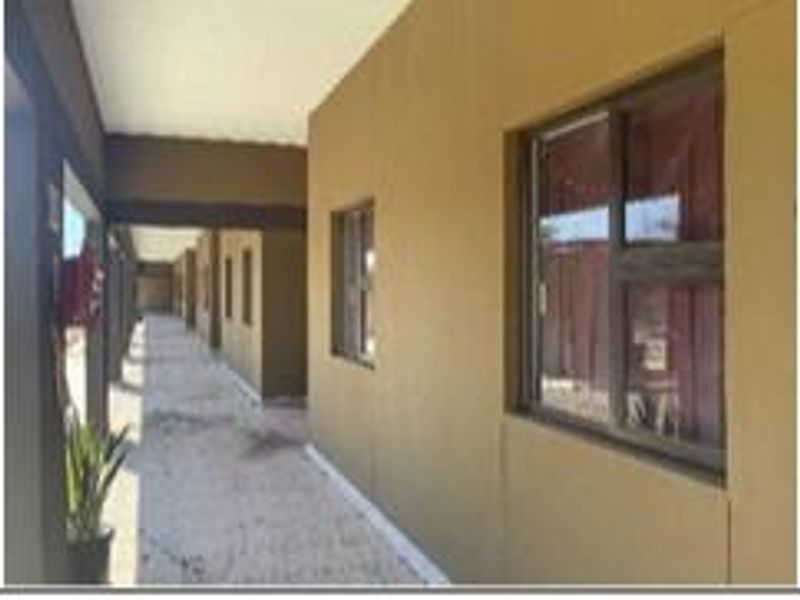 A covered exterior walkway or patio area featuring concrete flooring and aluminium window frames along the building facade.