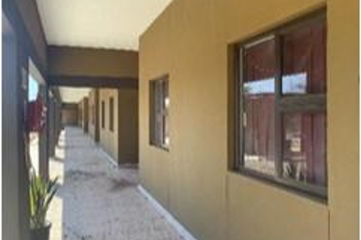 A covered exterior walkway or patio area featuring concrete flooring and aluminium window frames along the building facade.