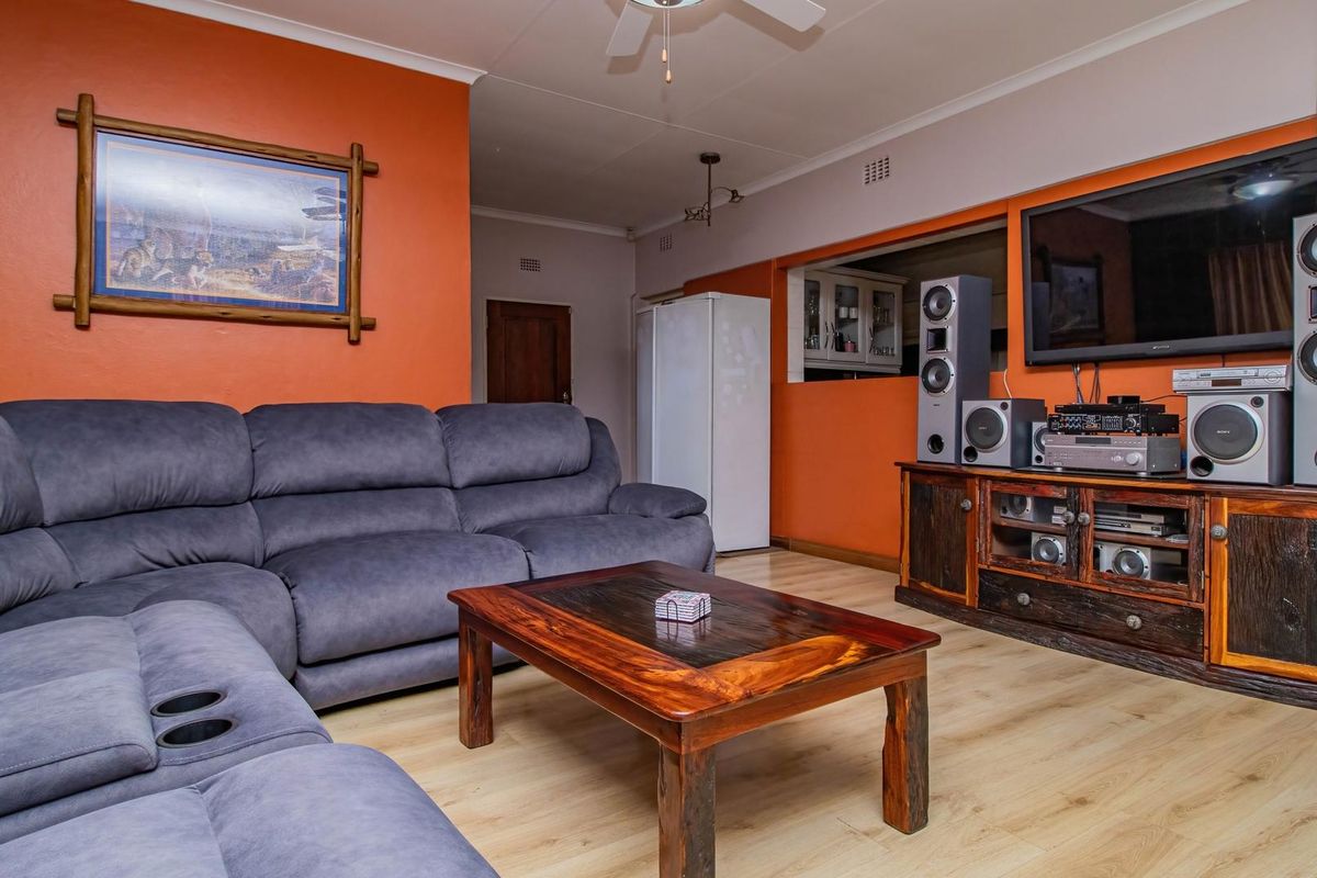 A living room featuring light wood-look laminate flooring, orange painted walls, and a pass-through window connecting to the kitchen area.