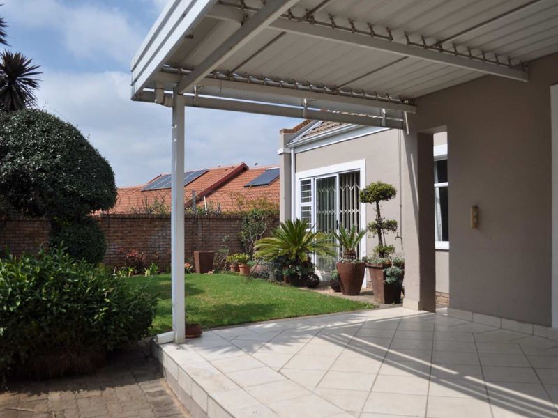 A covered patio area with tiled flooring, leading out to a private garden with a brick boundary wall and established landscaping.