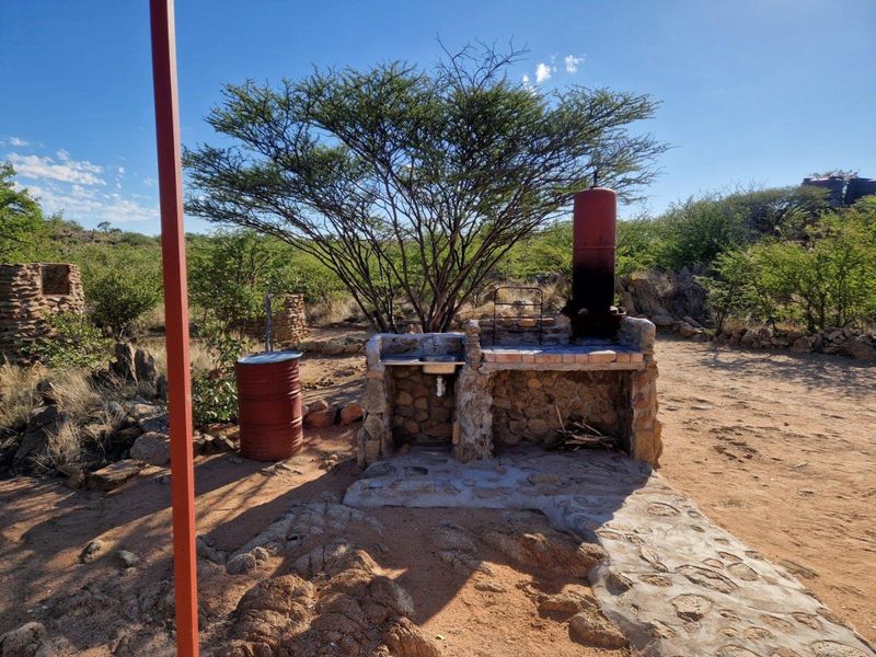 Outdoor stone-built braai area featuring an integrated sink and chimney, set within a natural lodge landscape.