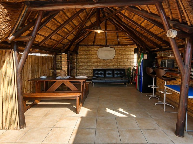 A spacious covered outdoor entertainment area featuring a traditional thatched roof, exposed timber structure, brick walling, and a built-in bar counter.