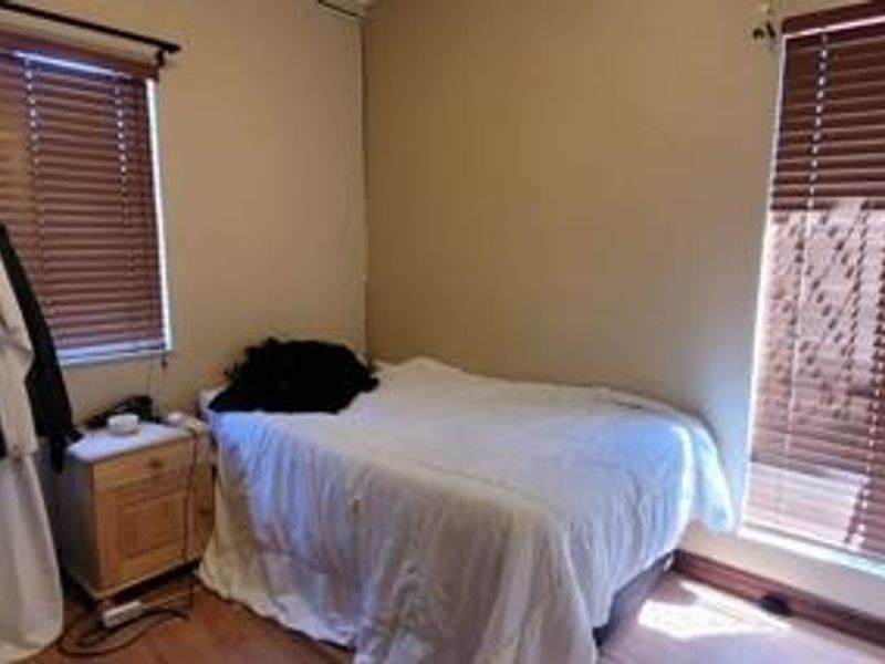 A standard bedroom featuring laminate flooring and dual windows with fitted venetian blinds, offering a functional space with neutral wall tones.