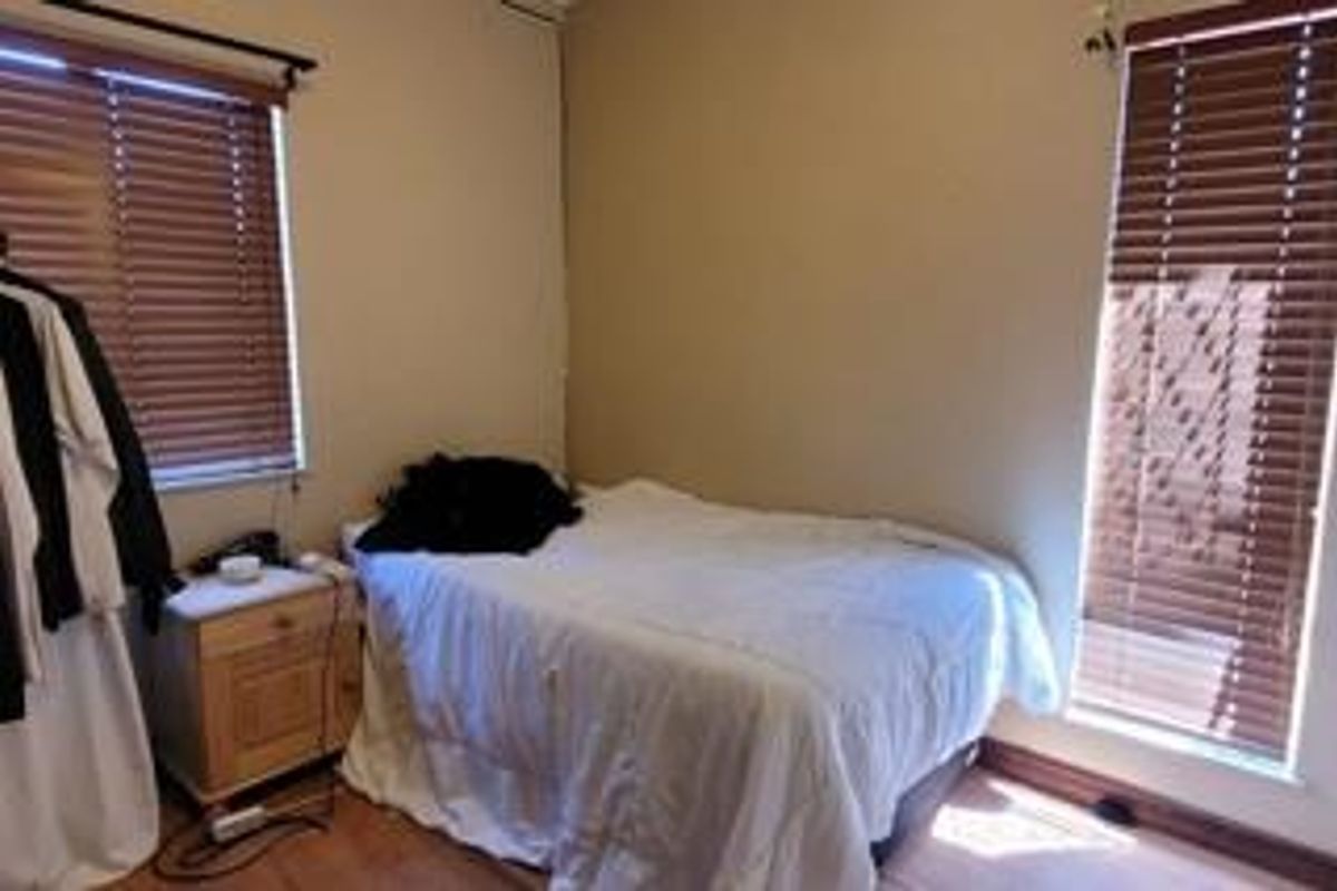 A standard bedroom featuring laminate flooring and dual windows with fitted venetian blinds, offering a functional space with neutral wall tones.
