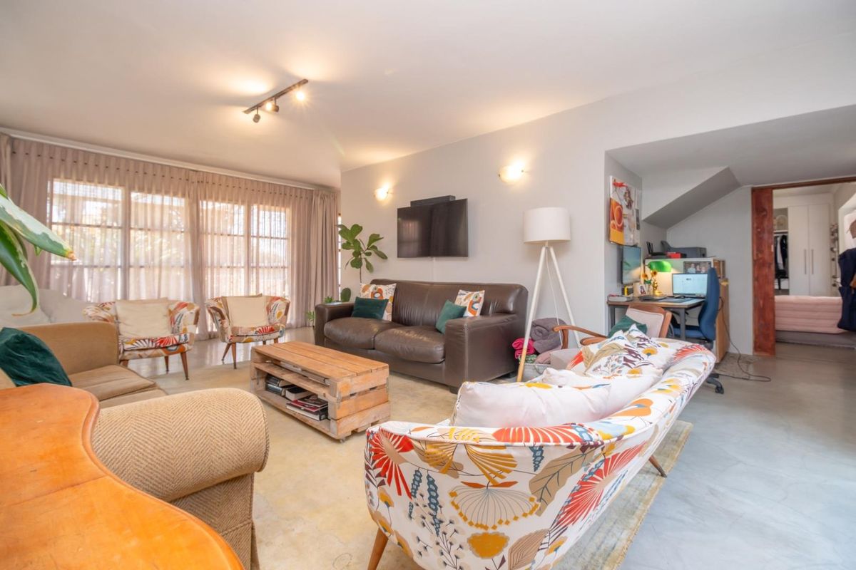 Spacious living room featuring polished concrete floors, track lighting, and wall sconces, with an open-plan layout leading to a secondary area.
