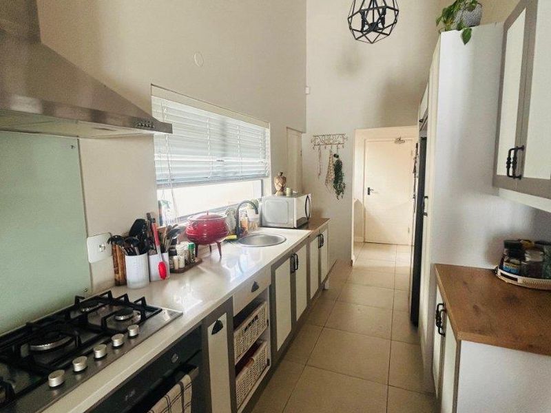 Modern galley-style kitchen featuring stone countertops, gas cooktop, stainless steel extractor, and high vaulted ceilings with contemporary pendant lighting.