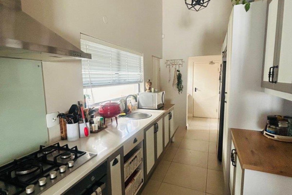 Modern galley-style kitchen featuring stone countertops, gas cooktop, stainless steel extractor, and high vaulted ceilings with contemporary pendant lighting.