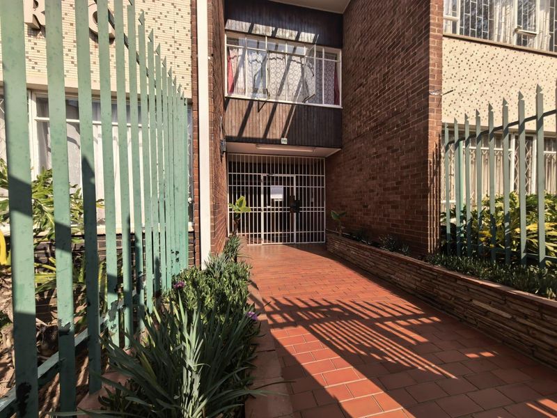 Front entrance of the apartment building featuring a brick facade, secure metal gate, and a tiled walkway with integrated planter boxes.