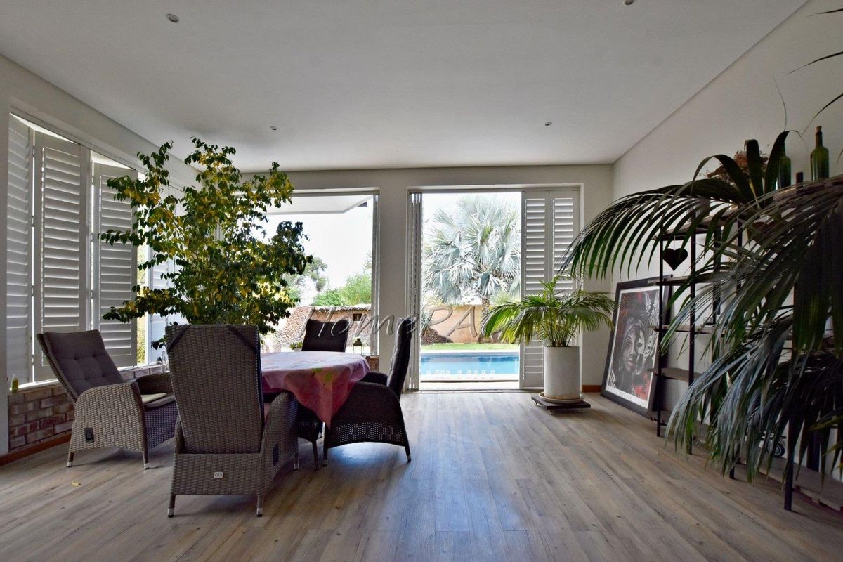 Bright living area featuring wood-look flooring, recessed lighting, and large folding doors opening to a patio and pool area.