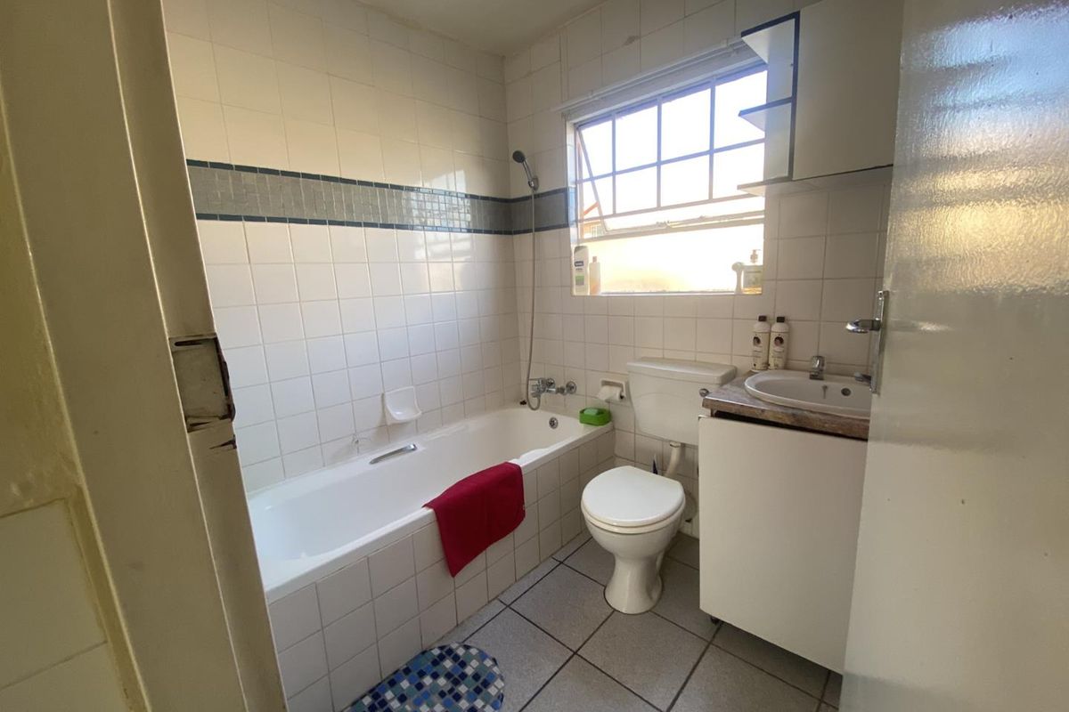 A dated bathroom featuring a standard bathtub, toilet, and vanity basin with tiled walls and flooring.