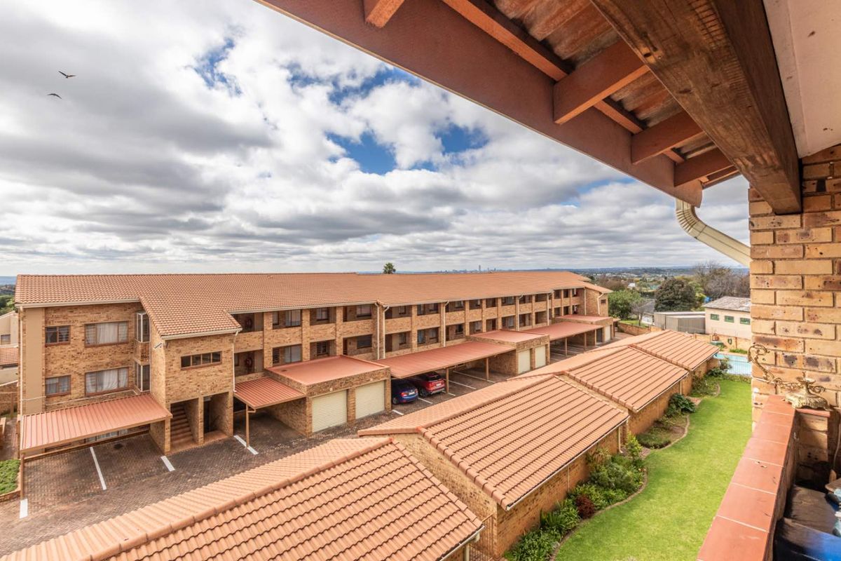 Elevated view overlooking the apartment complex, featuring face-brick architecture, tiled roofing, covered parking bays, and landscaped garden areas.