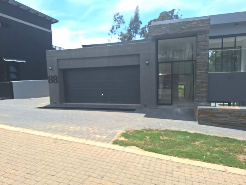 Modern cluster home exterior featuring a double garage, stone cladding accents, and a paved driveway entrance.
