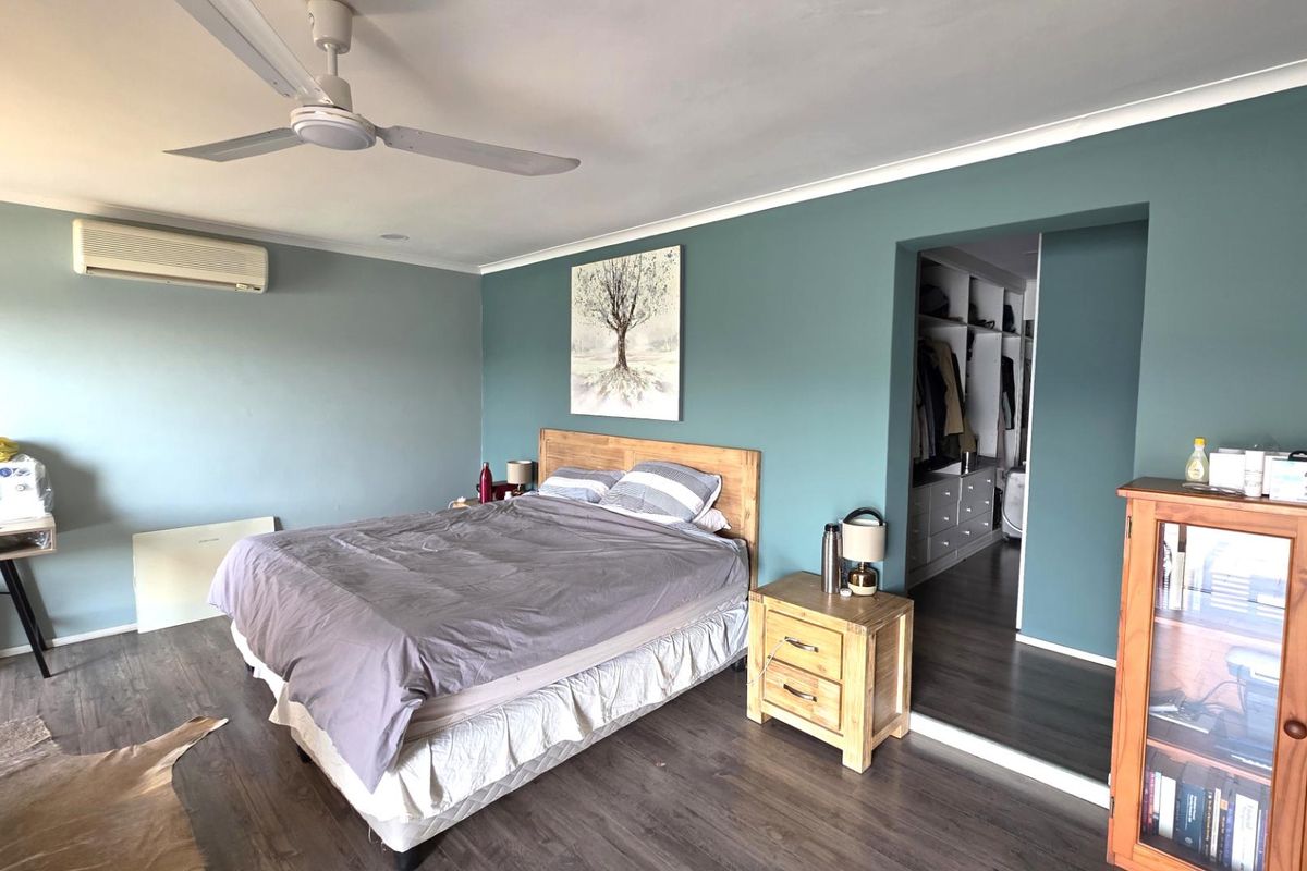 Spacious bedroom featuring a walk-in wardrobe, split system air conditioning, ceiling fan, and modern laminate flooring.