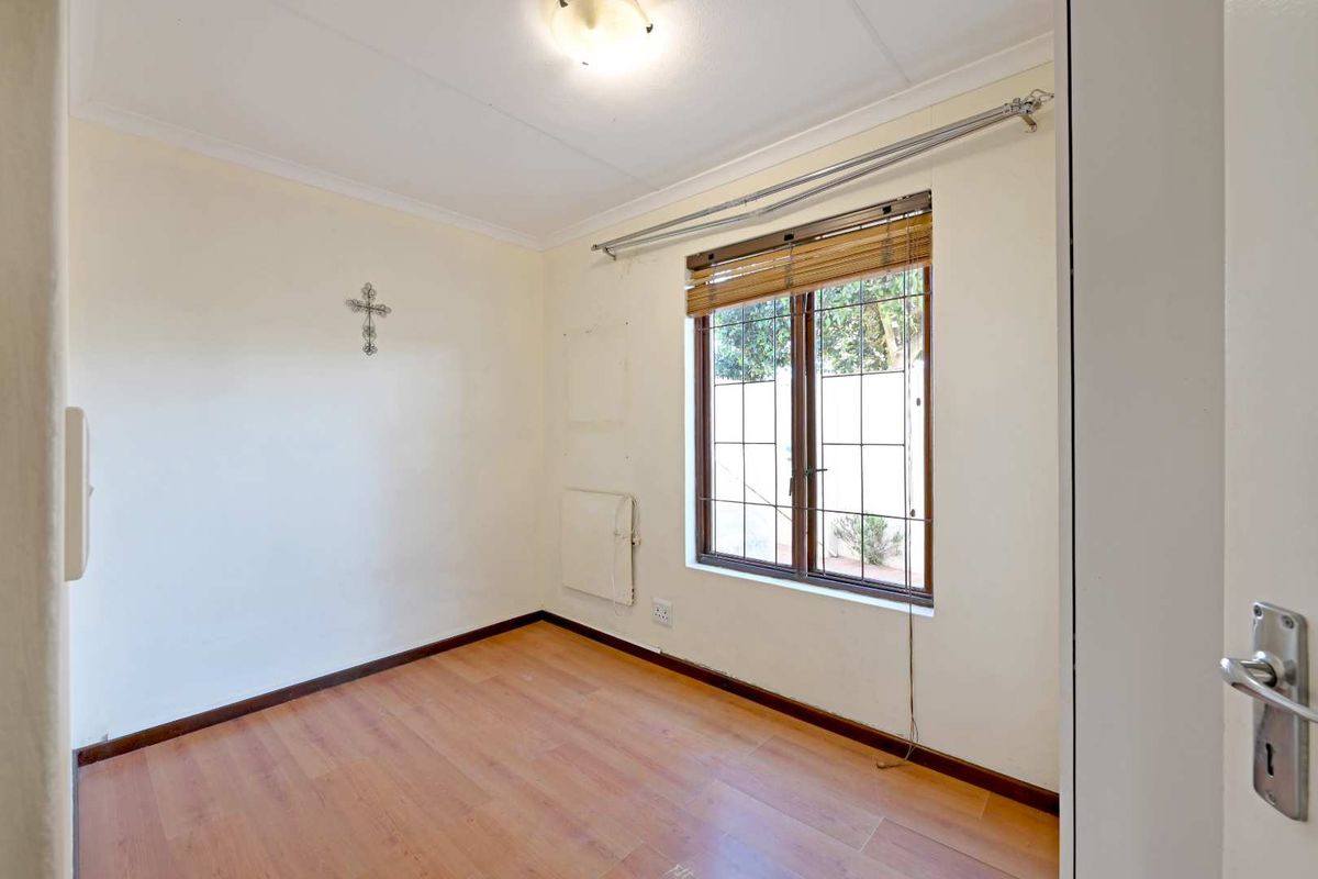 An empty bedroom featuring laminate flooring, a window with security bars, and a wall-mounted heater, ready for personalization.