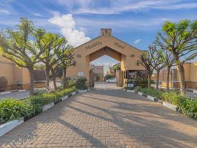 The main entrance gate to the residential cluster complex, featuring a paved driveway and established landscaping.