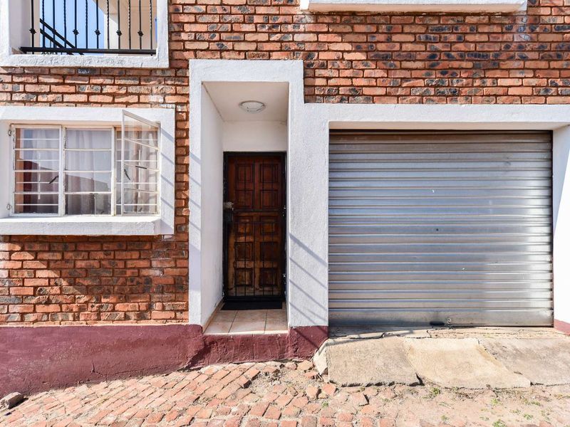 Front elevation of a townhouse featuring exposed brickwork, a secure timber entrance door, and a single roller garage door with a concrete driveway.