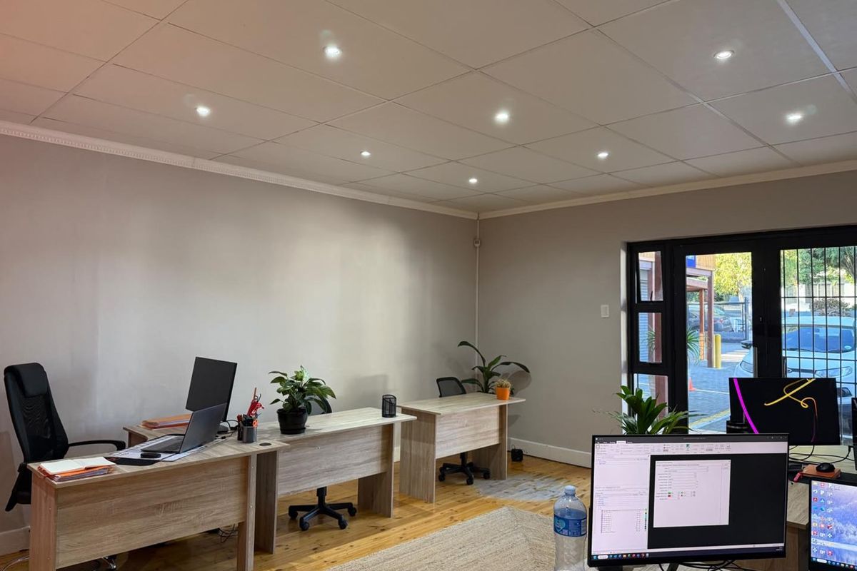 A functional office space featuring timber flooring, recessed downlighting, and a glass panel door providing natural light and exterior access.
