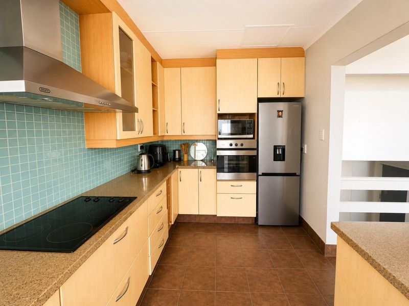 A functional kitchen featuring light wood cabinetry, stone-look countertops, blue mosaic tile backsplash, and integrated stainless steel appliances.