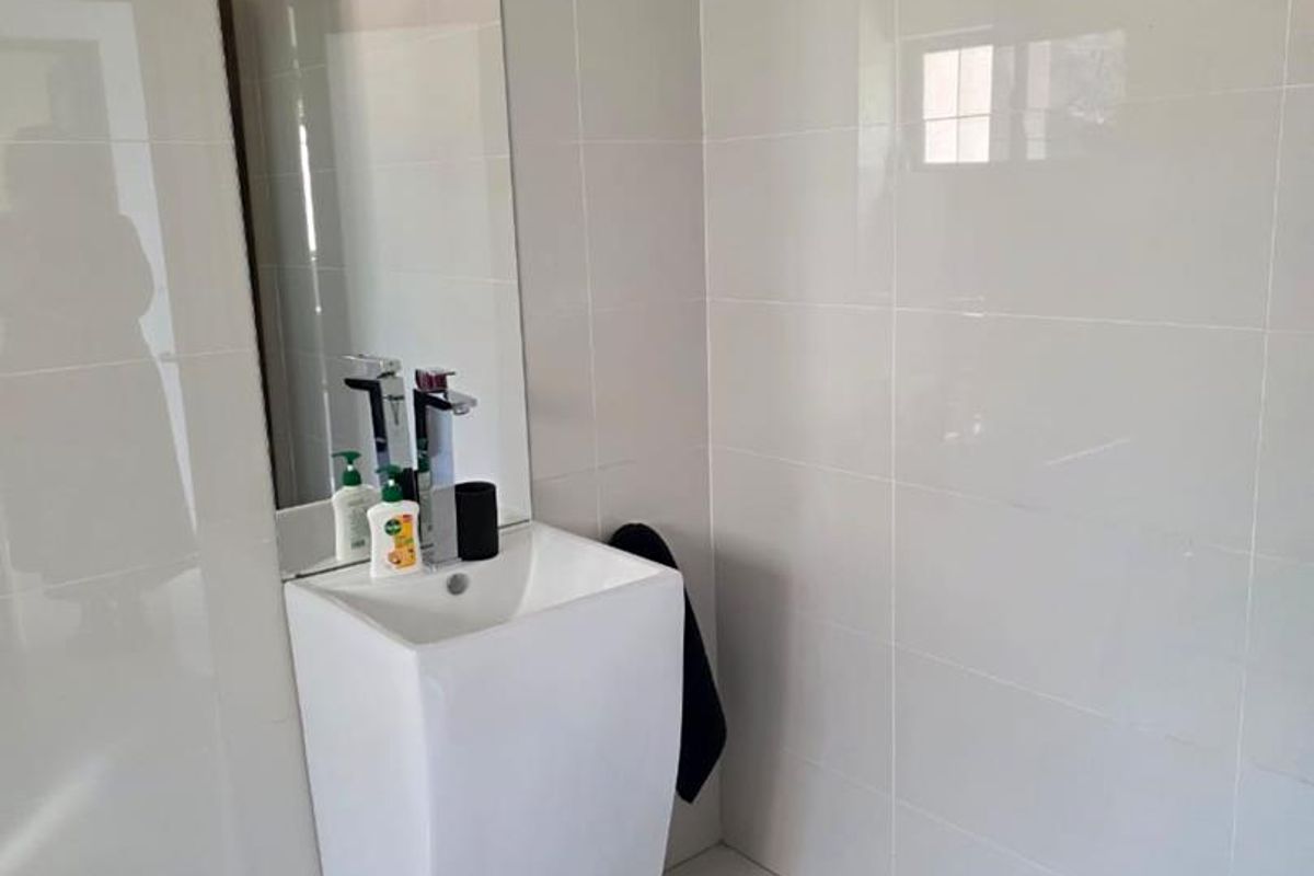 A clean and modern bathroom featuring a minimalist pedestal basin, chrome mixer tap, large wall-mounted mirror, and neutral ceramic tiling throughout.