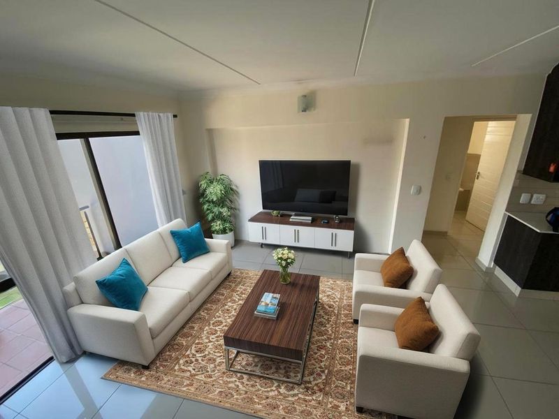 An open-plan living area featuring tiled floors, neutral walls, and a sliding glass door leading to an outdoor space, adjacent to a kitchen area.