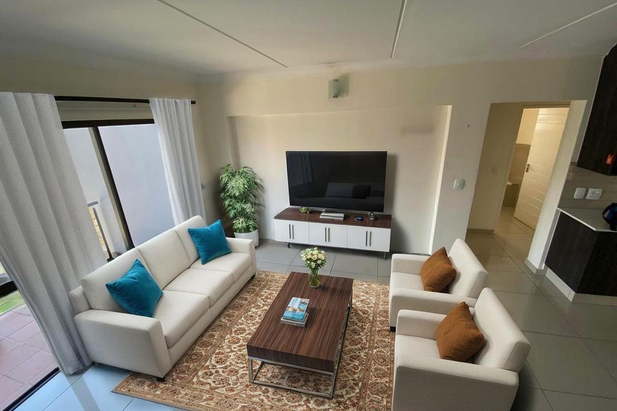 An open-plan living area featuring tiled floors, neutral walls, and a sliding glass door leading to an outdoor space, adjacent to a kitchen area.