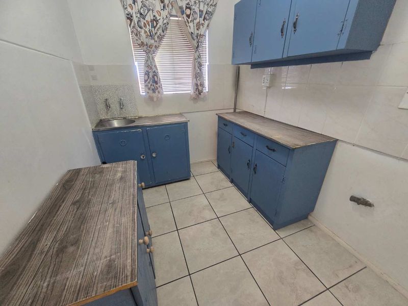 A functional laundry room featuring built-in blue cabinetry, laminate countertops, a stainless steel sink, and tiled flooring.