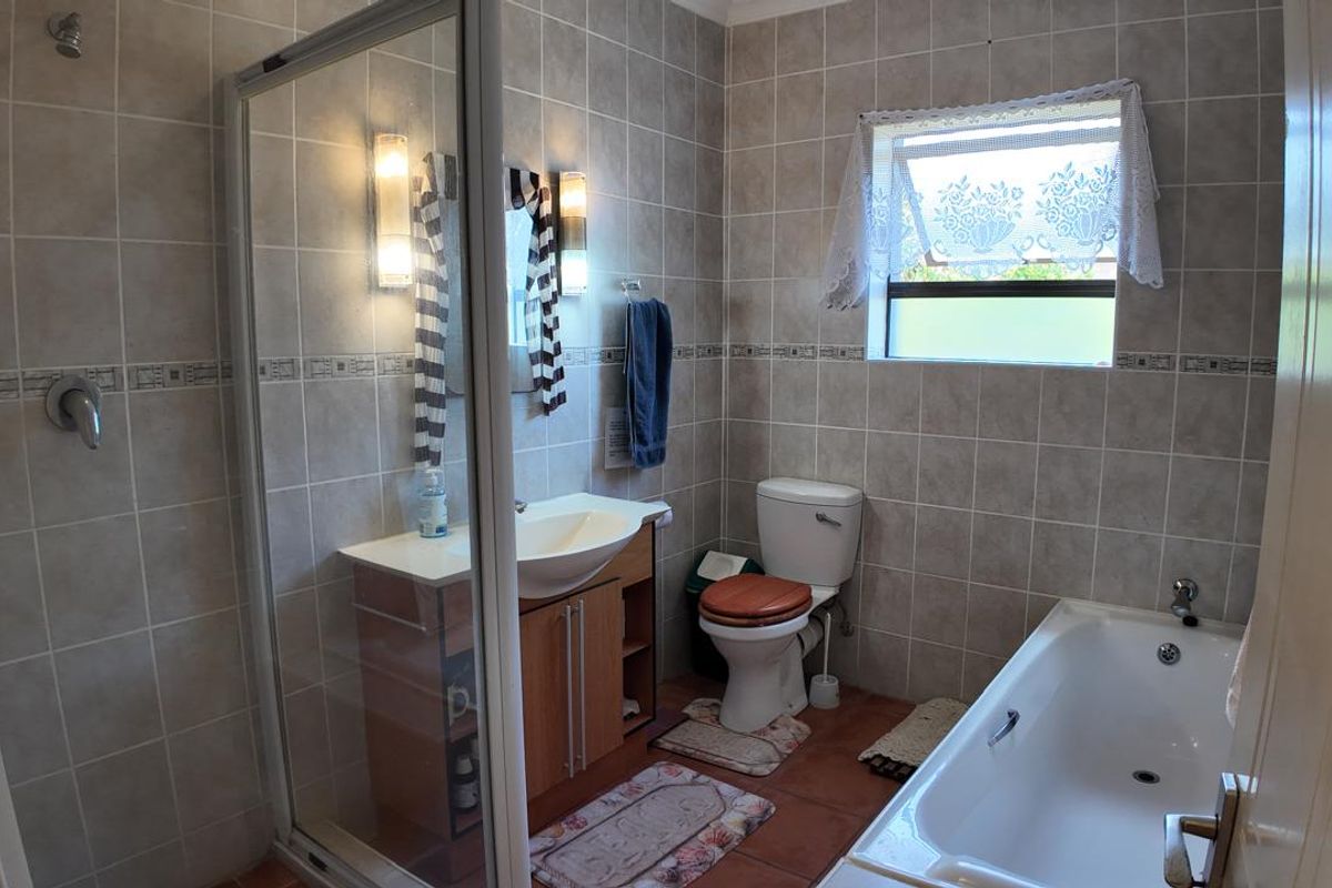 A functional bathroom featuring a glass-enclosed shower, a built-in vanity, a standard toilet, and a bathtub with neutral wall tiling.