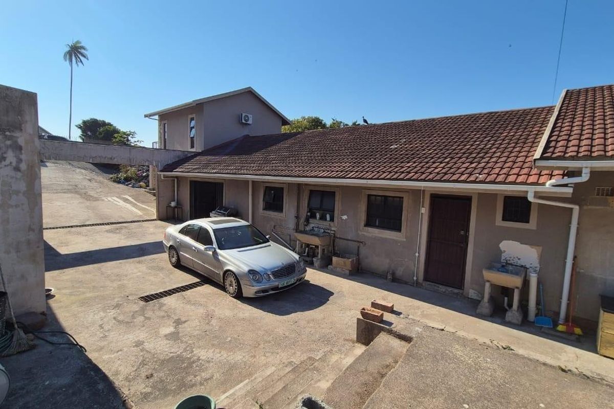 Rear exterior view of the property featuring a concrete driveway, tiled roof, and external utility wash basins against a weathered plaster facade.