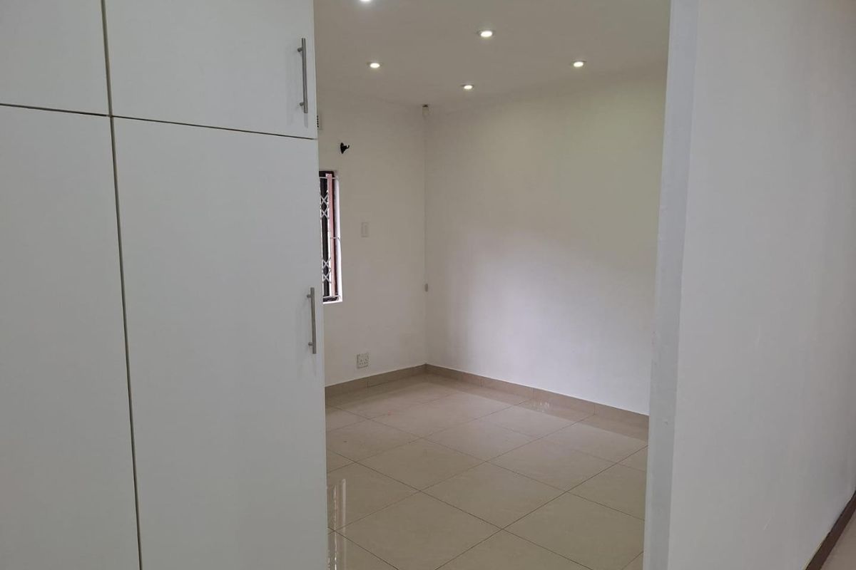 A clean, empty bedroom featuring neutral tiled flooring, built-in cupboards, and modern recessed downlighting.