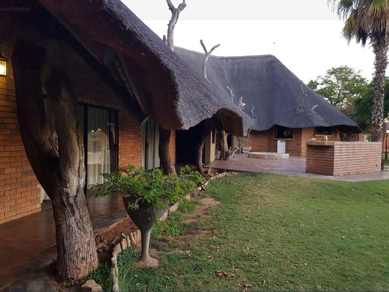 Rear view of a farm-style residence featuring a traditional thatch roof, face brick exterior, and a spacious patio area overlooking the garden.