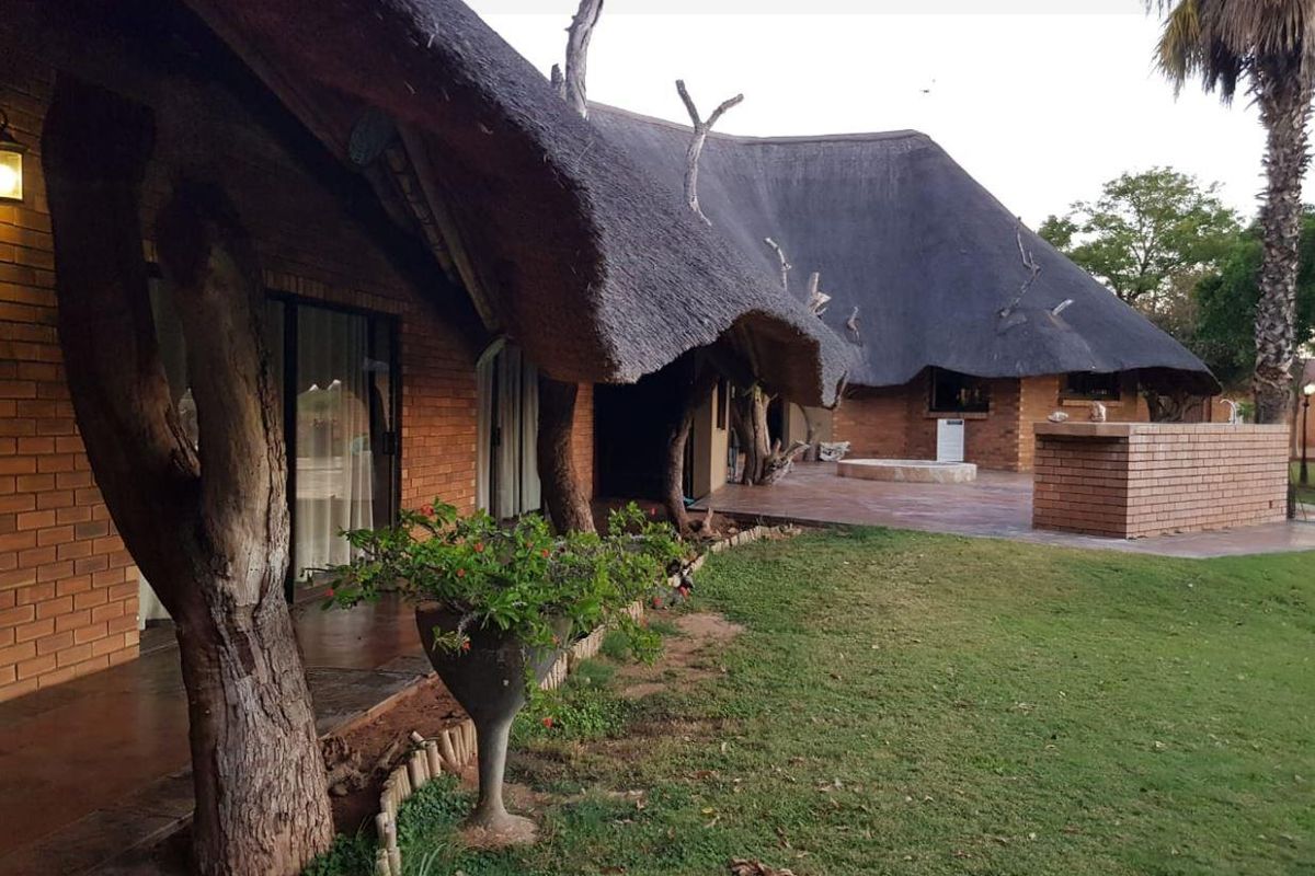 Rear view of a farm-style residence featuring a traditional thatch roof, face brick exterior, and a spacious patio area overlooking the garden.