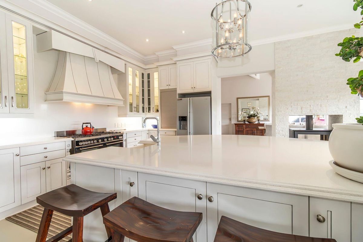 A modern, well-appointed kitchen featuring a large central island with stone countertops, custom cabinetry, a built-in range, and elegant pendant lighting.