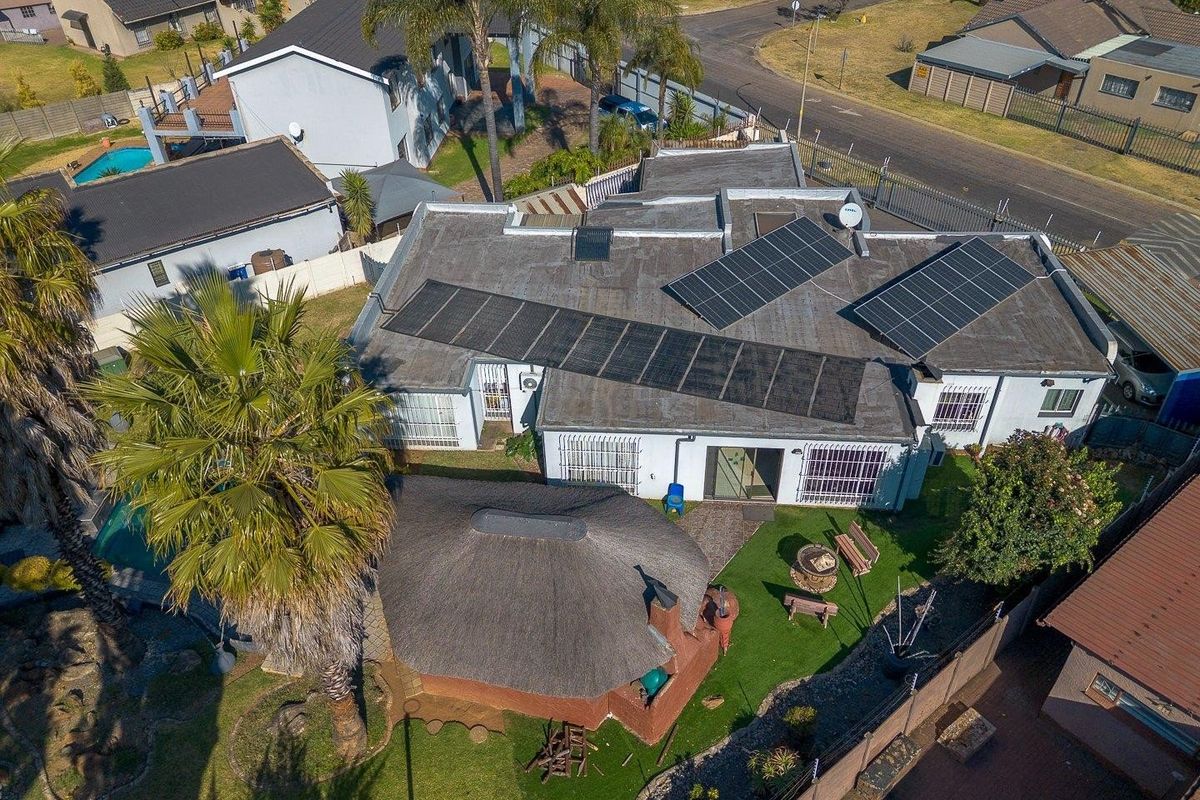 Aerial view of the property featuring a flat roof with solar panel installation, a detached thatched lapa, and a landscaped garden area.