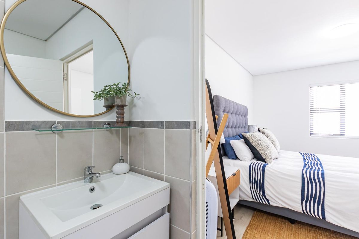 A modern bathroom vanity with a circular mirror, adjacent to a bright, well-lit bedroom with neutral finishes.