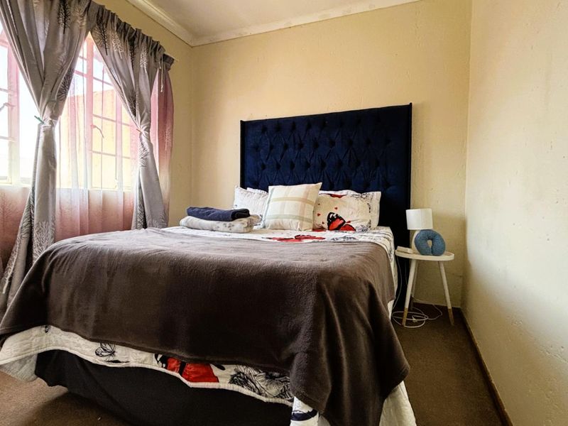 A bedroom featuring carpeted flooring and a window, showing signs of wear on the wall surfaces.