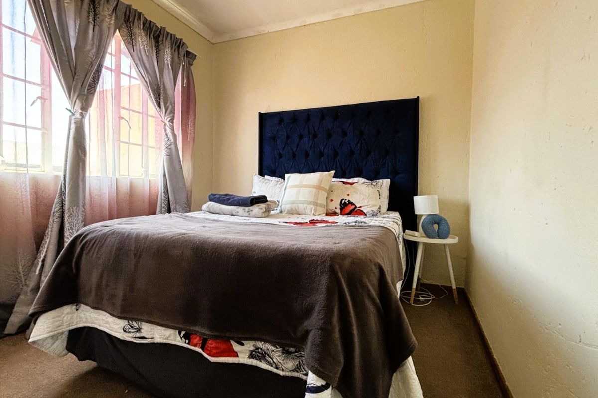 A bedroom featuring carpeted flooring and a window, showing signs of wear on the wall surfaces.
