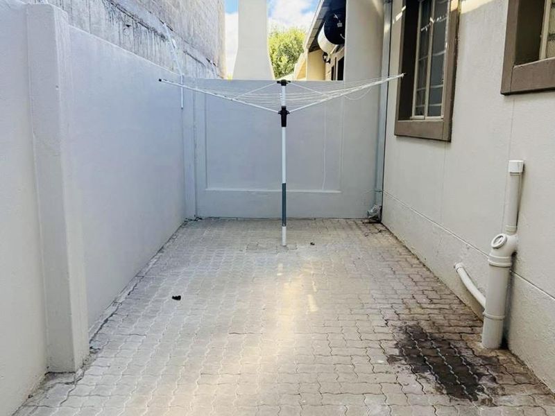 A paved rear courtyard area featuring boundary walls and external plumbing, providing a functional utility space for the townhouse.