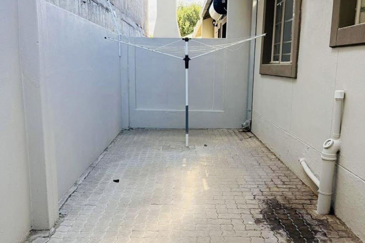 A paved rear courtyard area featuring boundary walls and external plumbing, providing a functional utility space for the townhouse.