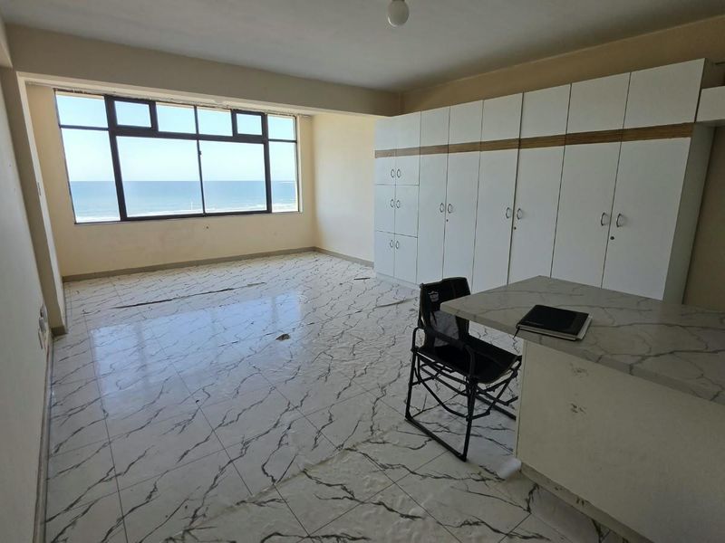 Spacious bedroom featuring built-in cupboards, tiled flooring, and expansive ocean views. The room is vacant and ready for renovation or staging.
