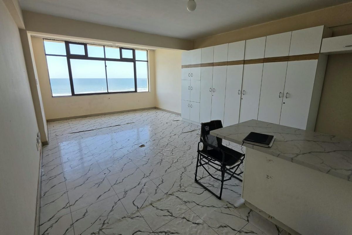 Spacious bedroom featuring built-in cupboards, tiled flooring, and expansive ocean views. The room is vacant and ready for renovation or staging.