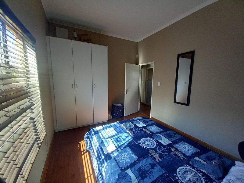 A functional bedroom featuring laminate flooring, a built-in wardrobe, and venetian blinds, offering a neutral base for personalization.