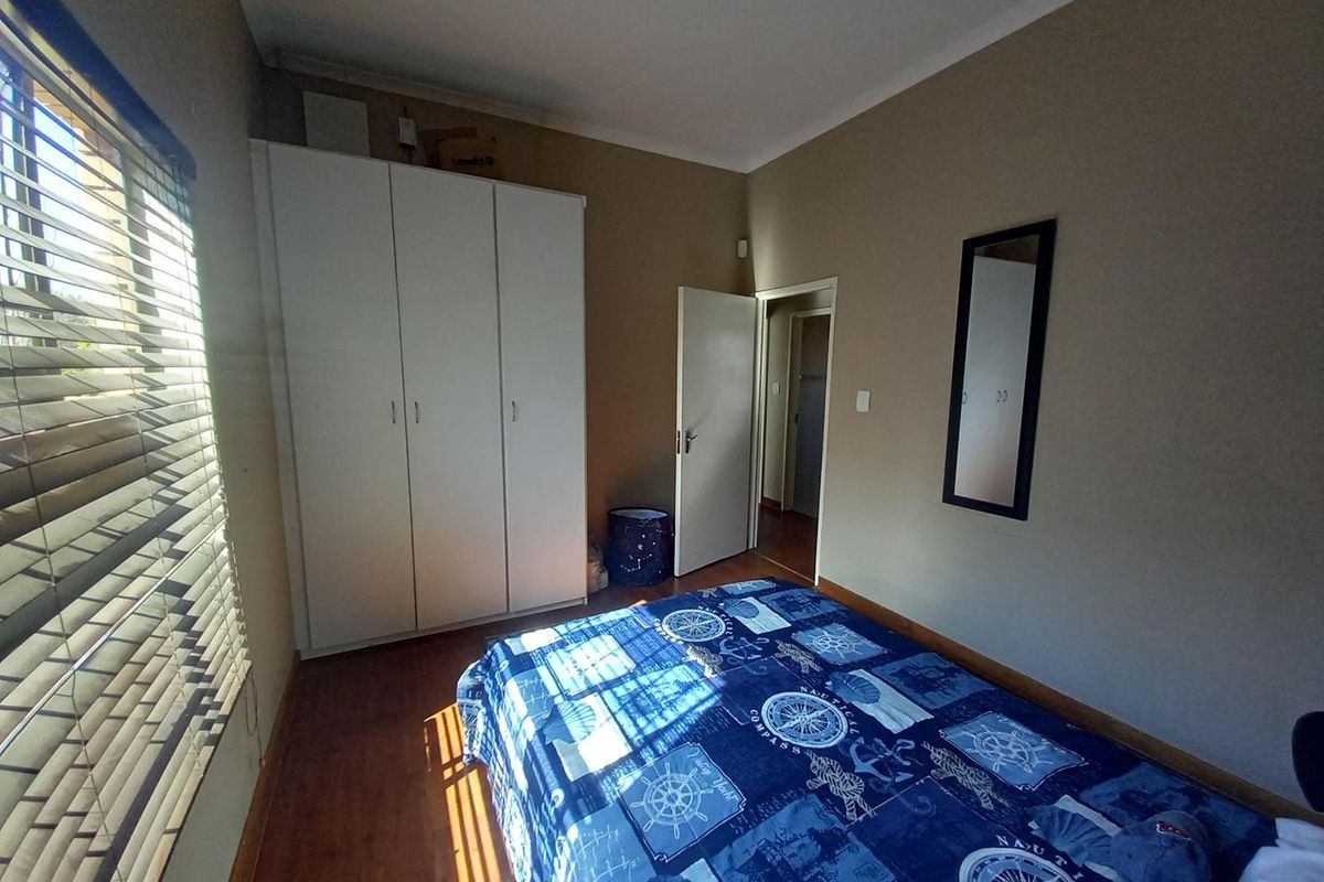 A functional bedroom featuring laminate flooring, a built-in wardrobe, and venetian blinds, offering a neutral base for personalization.