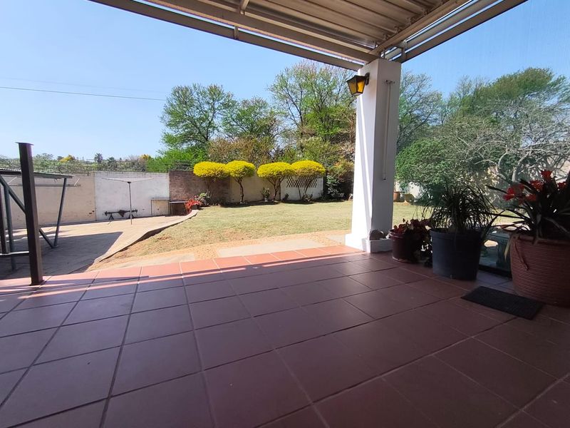 A covered patio area with tiled flooring overlooking a private garden with a brick boundary wall and established trees.