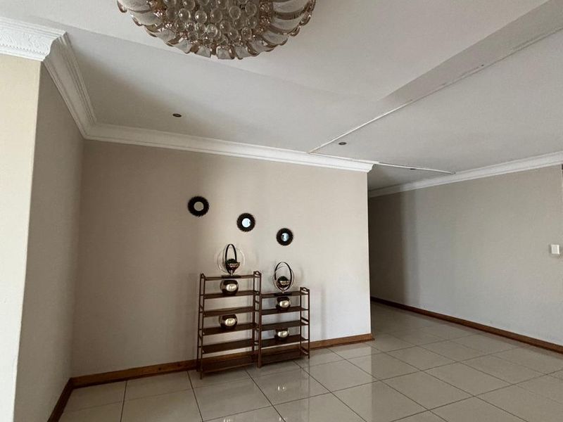 A spacious living area featuring neutral walls, tiled flooring, crown molding, and an ornate central ceiling light fixture.