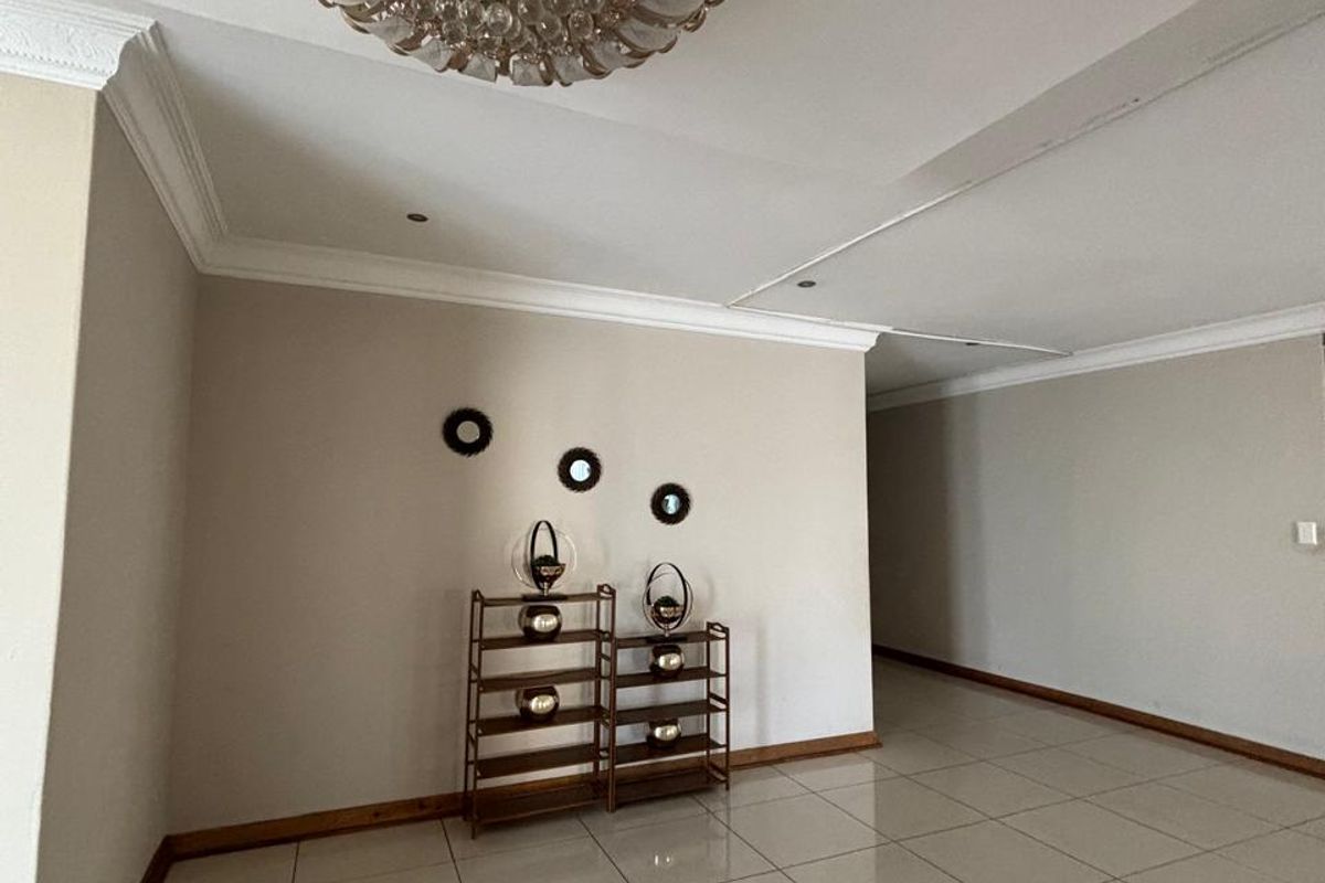 A spacious living area featuring neutral walls, tiled flooring, crown molding, and an ornate central ceiling light fixture.