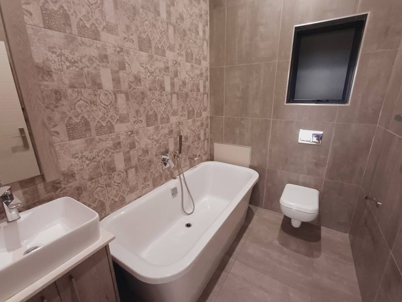 Modern bathroom featuring a freestanding bathtub, wall-mounted toilet, vanity basin, and stylish patterned wall tiling with neutral floor tiles.