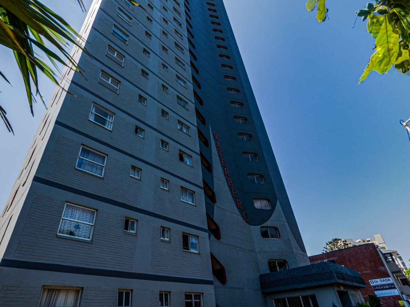Low angle view of a multi-story apartment building facade featuring grey brickwork and multiple window units.