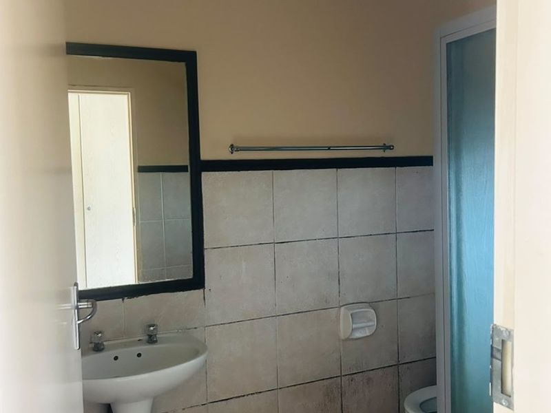 A functional bathroom featuring a pedestal basin, shower enclosure, and tiled finishes, currently requiring cosmetic updates to address tile staining and wear.