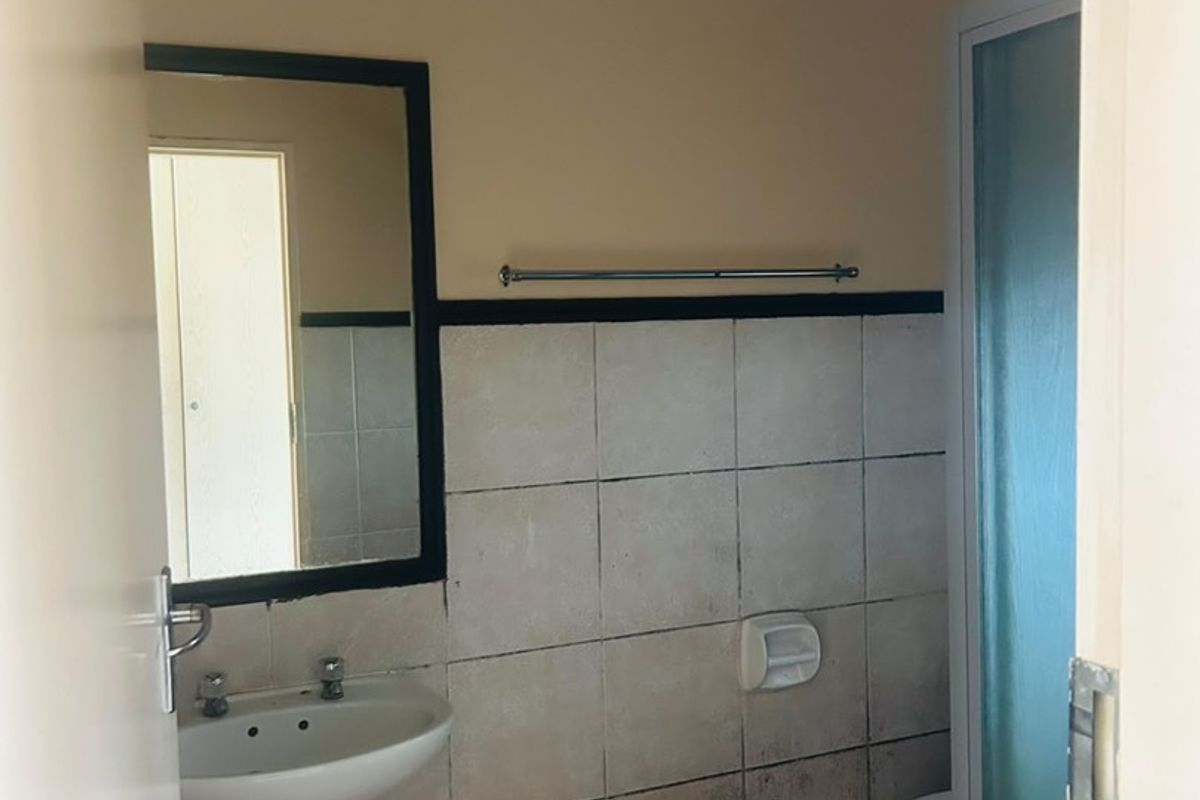 A functional bathroom featuring a pedestal basin, shower enclosure, and tiled finishes, currently requiring cosmetic updates to address tile staining and wear.